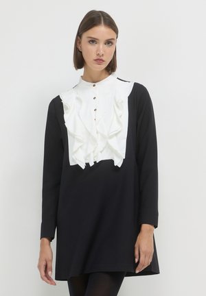 Schwarzes Kleid mit langen Ärmeln und einem weißen, rüschierten Vorderteil, ausgestattet mit einem hohen Kragen und Knöpfen, glatter Textur und knielanger Schnitt.