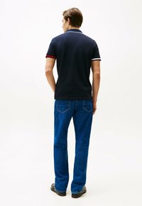 Polo shirt blu navy con rifiniture del colletto rosso e bianco a contrasto; abbinato a jeans in denim blu. Design semplice, maniche corte, vestibilità classica.