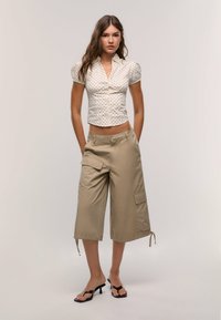 Short-sleeve, cream blouse with black polka dots; beige, cargo-style pants with pockets; black heeled sandals; relaxed fit.