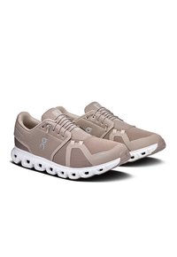 Light brown athletic shoes made of mesh with a textured surface, featuring a white sole with rounded cutouts and grey branding details.