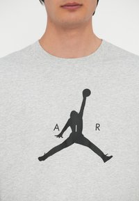 Graues Baumwoll-T-Shirt mit einem großen schwarzen Air Jordan Silhouette-Druck, darunter die Buchstaben "A", "I" und "R".