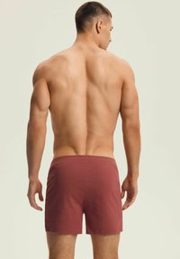 Bordowe kąpielówki z wygodnym elastycznym pasem, wykonane z gładkiego materiału, o prostym wzorze i krótkim kroju.