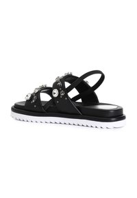 Sandalias negras con suela blanca gruesa, con adornos brillantes y diseño de tiras cruzadas. Fabricadas en cuero suave con una suela texturizada.