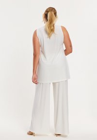 Weißes ärmelloses Top mit lockerem Sitz, kombiniert mit weißen Hosen mit weitem Bein. Der Stoff hat eine glatte, fließende Textur. Schlichtes Design, eleganter Look.