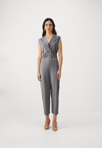 Grå ermeløs jumpsuit med skreddersydd design, belted midje og doble knapper. Jevn tekstur med tapered ben og sidelommedetalj.