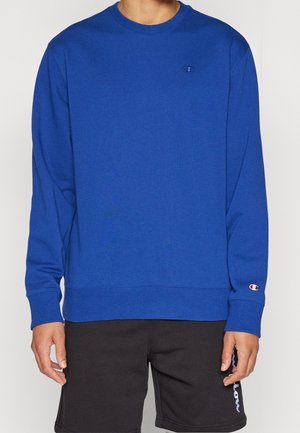 Felpa blu con maniche lunghe e girocollo. Presenta un logo sul petto e polsini e orlo a costine. Abbinata a pantaloni scuri.