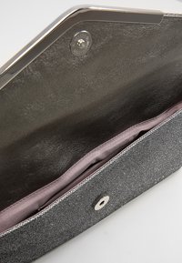 Pochette en tissu gris avec une fermeture métallique. Intérieur lisse en violet clair, bordé d'un fil argenté le long du bord.