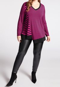 Lila och svart randig långärmad topp med V-ringning, med en asymmetrisk skärning, i kombination med svarta faux läderleggings och klackar.