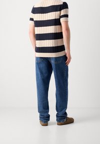 Pruhovaný pletený svetr v námořnické modři a béžové barvě, s krátkými rukávy, a volné modré džíny. Hnědé boty doplňují ležérní vzhled.