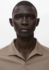 Camisa polo beige con cuello, mangas cortas y tejido texturizado, que presenta un diseño limpio y minimalista. Fondo liso.