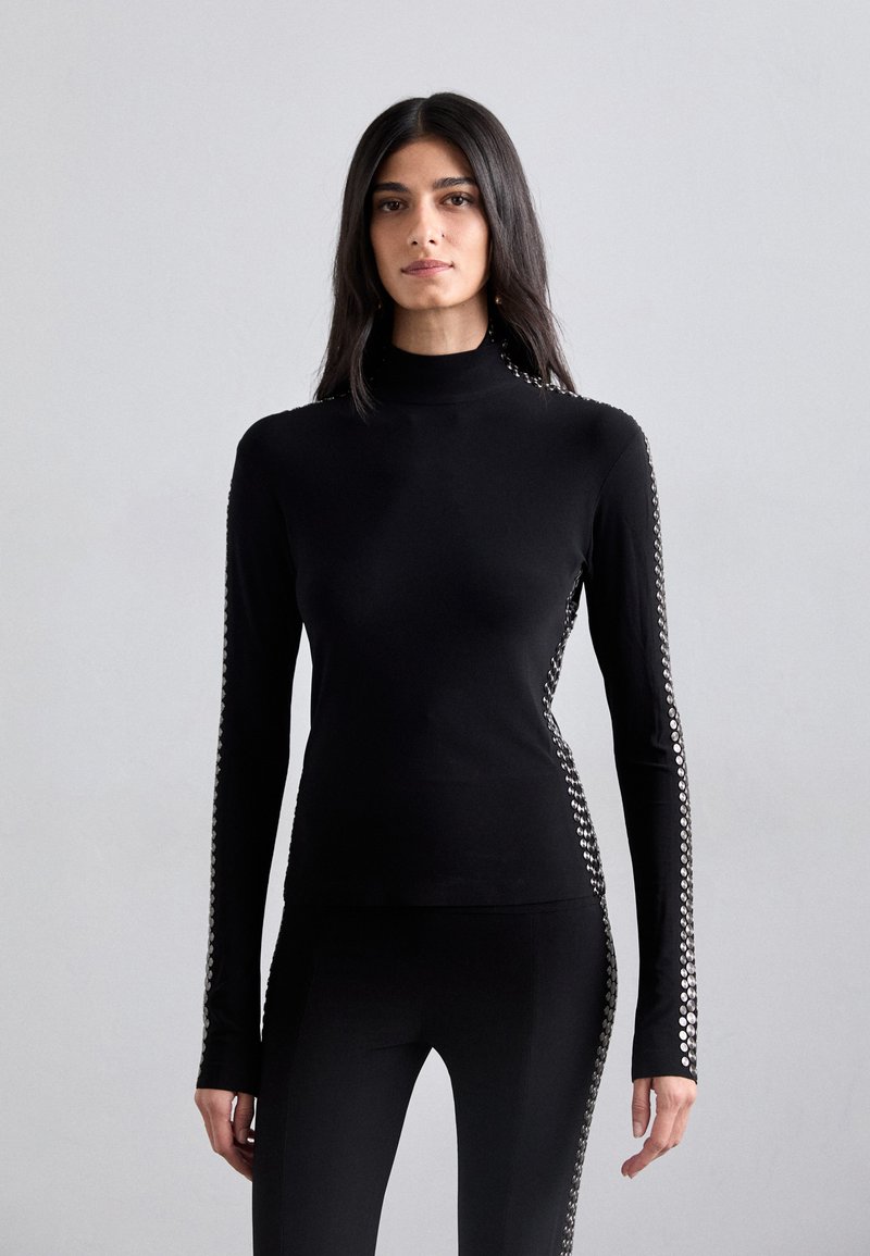 Black long-sleeve top with a mock neck, featuring metallic stud accents along the sleeves and a slim, fitted silhouette. Stretch fabric.