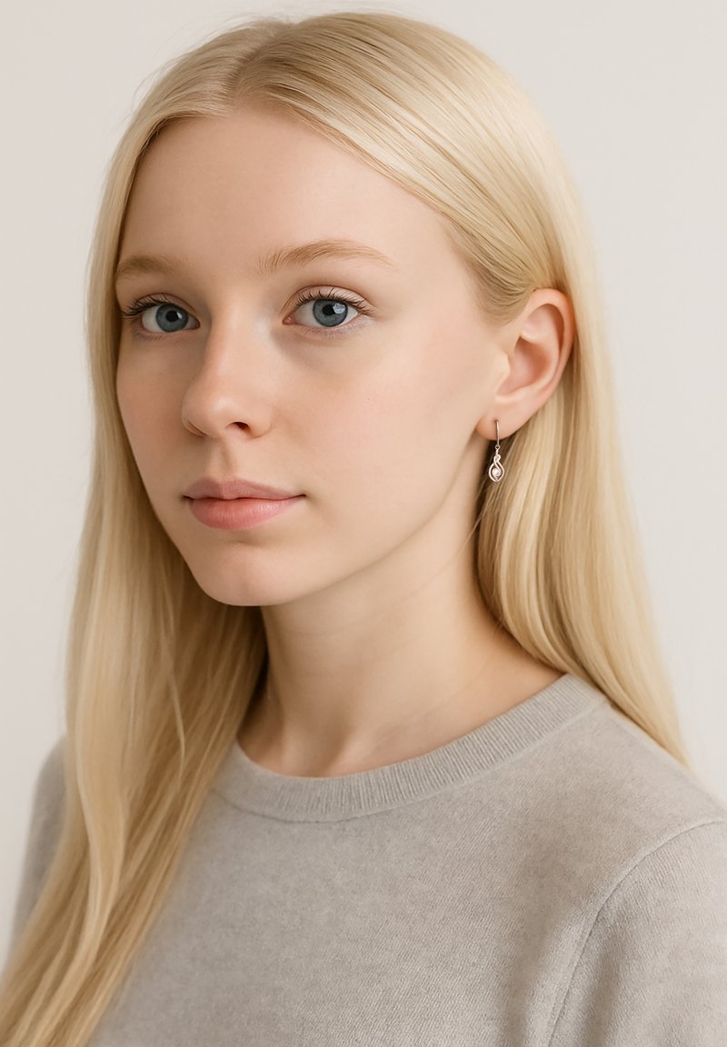 Silvriga tårformade örhängen hänger från modellens öron och har en delikat swirl-design. Modellen bär en ljusgrå tröja och har långt, rakt blont hår.