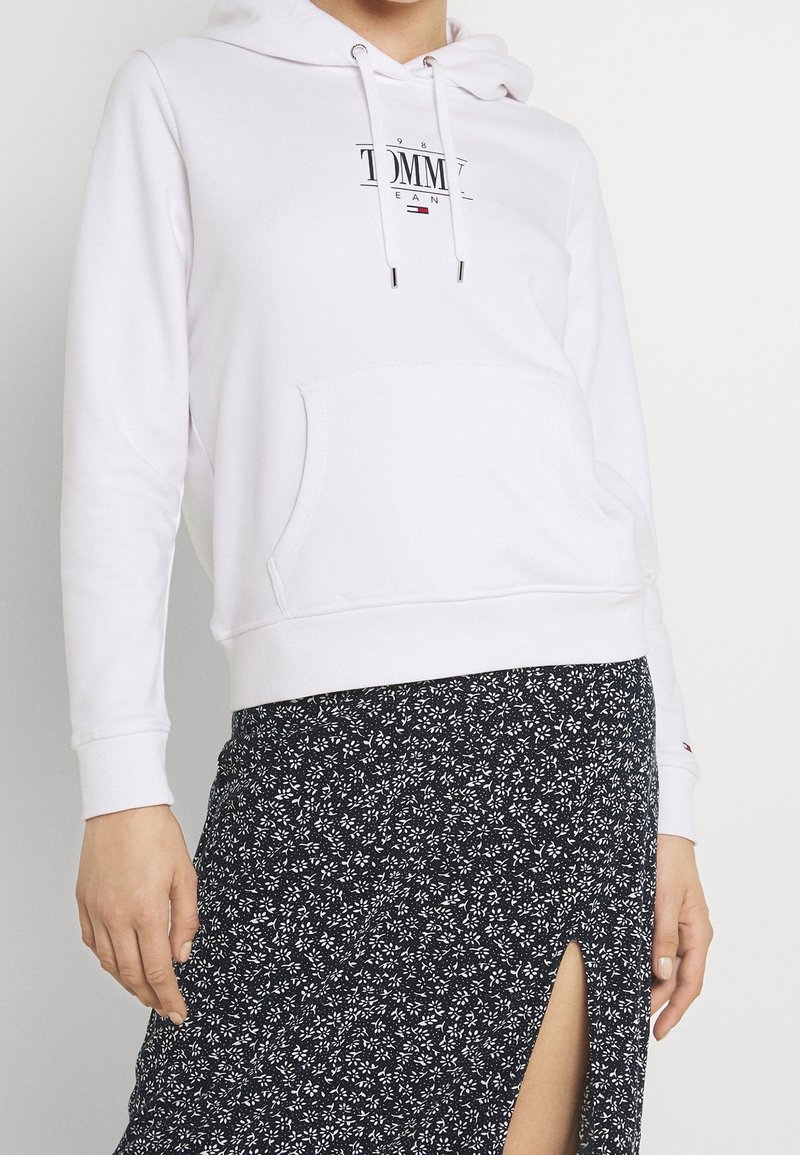 Bílá mikina s kapucí a přední kapsou, se šňůrkami. S potiskem loga "TOMMY". Kombinováno s černou sukní s květinovým vzorem a rozparkem.