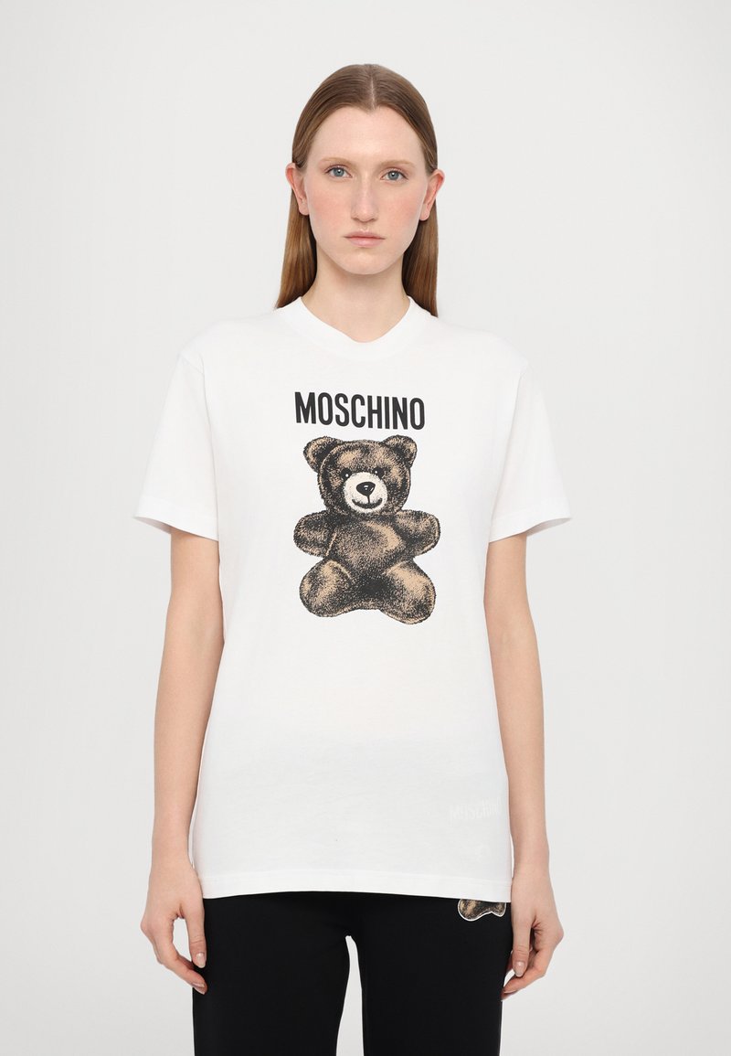 Hvit bomulls t-skjorte med en svart skisse av en bjørn og merkenavnet "MOSCHINO" over. Korte ermer og rund hals.