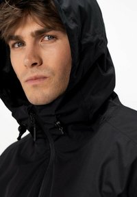 Černá voděodolná bunda s vysokým límcem a nastavitelnou kapucí. Obsahuje zipy a stahovací prvky pro lepší přizpůsobení. Hladká, strukturovaná tkanina.