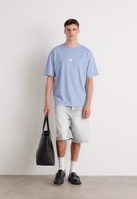 Ljusblå kortärmad t-shirt med logga, randiga denimshorts, svart tygväska, vita strumpor och svarta skor. Enkel, avslappnad outfit.