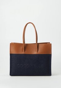 Brown leather handles on a navy blue fabric tote bag with a textured finish and embossed brand logo on the front.