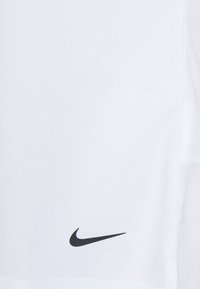 Hvit treningstrøye med en glatt tekstur. Har en svart Nike swoosh-logo nederst til venstre.