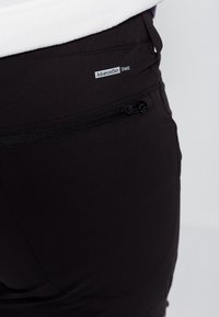 Svarta utomhusbyxor med en dragkedjeficka, AdvancedSkin Shield-märke och en slät, matt yta. Närbild av den bakre designen.