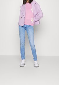 Fialový máčený kabát, růžový svetr s bílým květinovým vzorem, světlé modré džíny a bílé tenisky s černými pruhy.