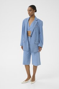 Denim blazer in light blue, single-button closure, two front pockets. Paired with matching knee-length shorts and a cropped top. Cream-colored shoes.