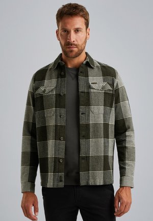 Chemise à carreaux verte et blanche en flanelle avec des boutons, deux poches poitrine, dotée d'un col et d'une texture douce. Pull noir en dessous.