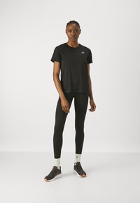 Black athletic t-shirt with short sleeves and New Balance logo, paired with black leggings and black sneakers featuring purple and orange accents.