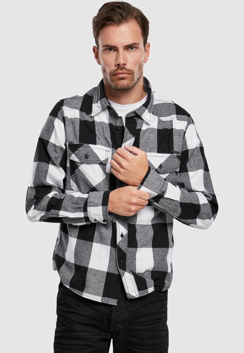 Zwart-wit geruite flanellen shirt met knoopsluiting aan de voorkant, twee borstzakken en lange mouwen met manchet. De stof lijkt textuur te hebben.