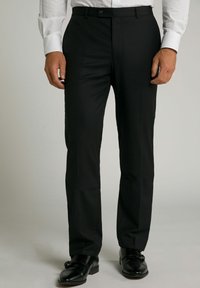Pantalones formales negros con un corte a medida, tejido suave, cierre de botón en la cintura y una línea marcada en la parte delantera. Llevados con zapatos de vestir negros.