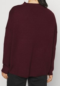 Maglione oversize bordeaux a maglia con superficie testurizzata e spalle cadenti, caratterizzato da maniche lunghe e una vestibilità rilassata.