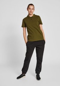 Grön pikétröja med korta ärmar, två knappar, ihopparad med svarta svettbyxor. Outfiten har en avslappnad passform och en avslappnad stil.