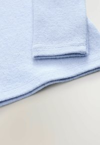 Indumento azzurro chiaro a maniche lunghe realizzato in un tessuto morbido e testurizzato, con orlo curvo e dettagli cuciti sulle maniche.