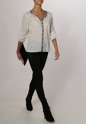 Hvid skjorte med dyb V-udskæring og grå kant, iført med sorte skinny jeans og sorte ankelstøvler med hæl.