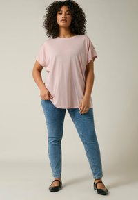 Ljusrosa kortärmad topp med en avslappnad passform och spetsdetaljer på axlarna, parat med blå smala jeans och svarta ballerinan.