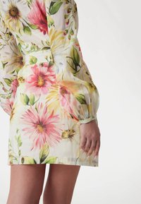 Kwiatowa sukienka z lekkiego, przezroczystego materiału w intensywne wzory różowych, żółtych i zielonych kwiatów; długie bufiaste rękawy z guzikami.