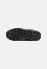 Rød sneakersåle med en sort gummiunderkonstruktion, der har et fiskebensmønster, glatte kanter og en afrundet tåform.