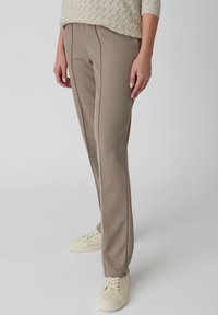 Beige op maat gemaakte broek in een textuurstof met een rechte pasvorm, voorzien van subtiele naaddetails en gecombineerd met lichtgekleurde sneakers.