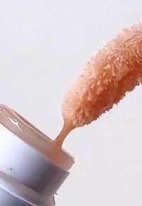 Pinceau applicateur de maquillage couvert de fond de teint liquide beige au-dessus d'un flacon de fond de teint ouvert sur un fond uni.