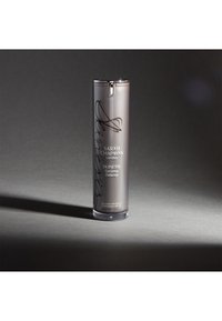Silberne zylindrische Pumpflasche mit klarem Boden, beschriftet mit "Sarah Chapman London" und "SKINESIS Dynamic Defence", mit elegantem Design.