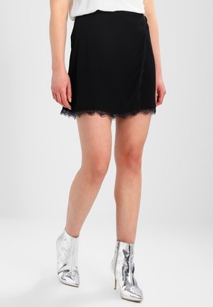 Mini gonna nera con orlo di pizzo, realizzata in tessuto morbido. Indossata con stivali alla caviglia argentati lucidi e una maglietta bianca. Design semplice con forma svasata.