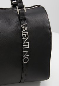 Svart syntetisk handväska med strukturerad yta, med en silverfärgad "VALENTINO"-logotyp som accent, dragkedjestängning och justerbar rem.