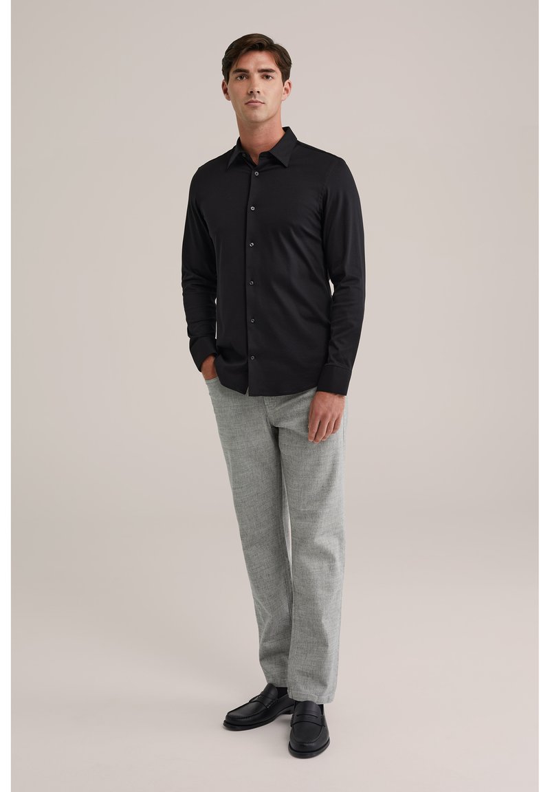 Juoda marškiniai su ilgomis rankovėmis, derinami su šviesiai pilkomis tekstūruotomis kelnėmis ir juodais slip-on batais. Paprasta fonas, be raštų.
