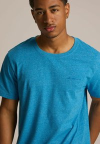 Niebieska krótko rękawowa koszulka wykonana z teksturowanej tkaniny, z okrągłym dekoltem i małym logo na lewej piersi.