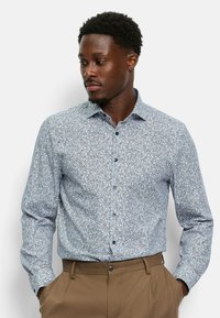 Chemise à boutons en tissu bleu clair avec un motif floral en swirl dans des teintes de bleu plus foncé et des accents rouges, dotée d'un col pointu et de manches longues.