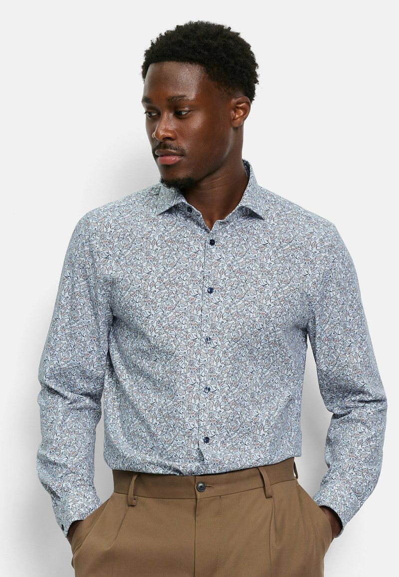Chemise à boutons en tissu bleu clair avec un motif floral en swirl dans des teintes de bleu plus foncé et des accents rouges, dotée d'un col pointu et de manches longues.
