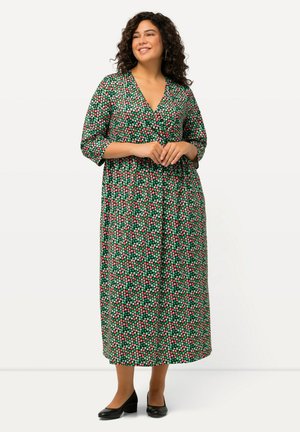 Maxikleid mit tiefem V-Ausschnitt, grüner Stoff mit roten und rosa Punkten. Verfügt über Dreiviertelärmel und einen lockeren Schnitt.