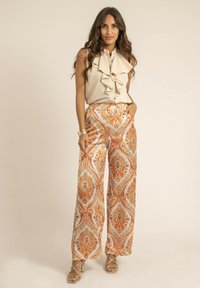 Blouse beige à volants avec boutons, associée à un pantalon large à imprimé paisley orange et doré. Tissu doux, coupe décontractée et design structuré.