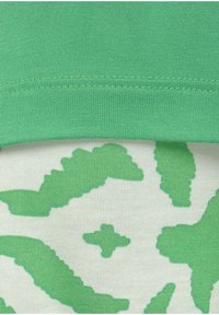 Grünes Baumwolltop mit strukturiertem, geripptem Ausschnitt und einem Druckdesign aus abstrakten grünen Formen auf einem hellen Hintergrund.