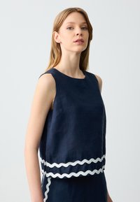 Marineblaues ärmelloses Oberteil aus Leinenstoff mit einem gewellten weißen Saum, runder Ausschnitt und lässiger Passform.
