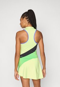 Αμάνικο αθλητικό φόρεμα σε ανοιχτό κίτρινο-πράσινο χρώμα με μαύρα και πράσινα γεωμετρικά σχέδια, διακοσμημένο με μπλε περιθώρια. Λείο, ελαστικό ύφασμα.